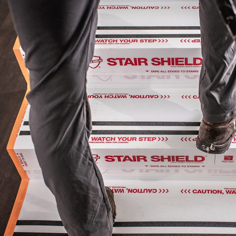A person walks up stairs protected by Stair Shield coverings, which feature warning messages to watch your step.